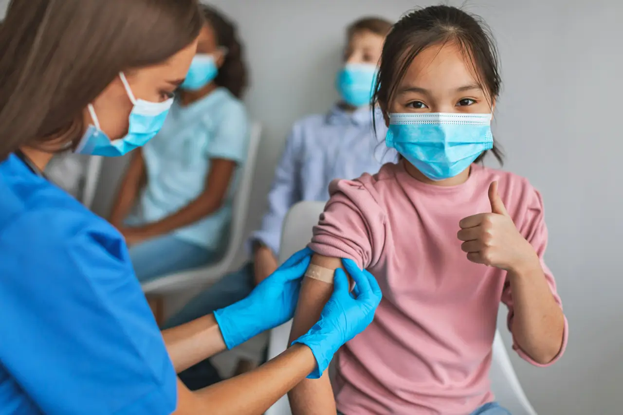 Doctor patching the arm of a young asain girl in a mask